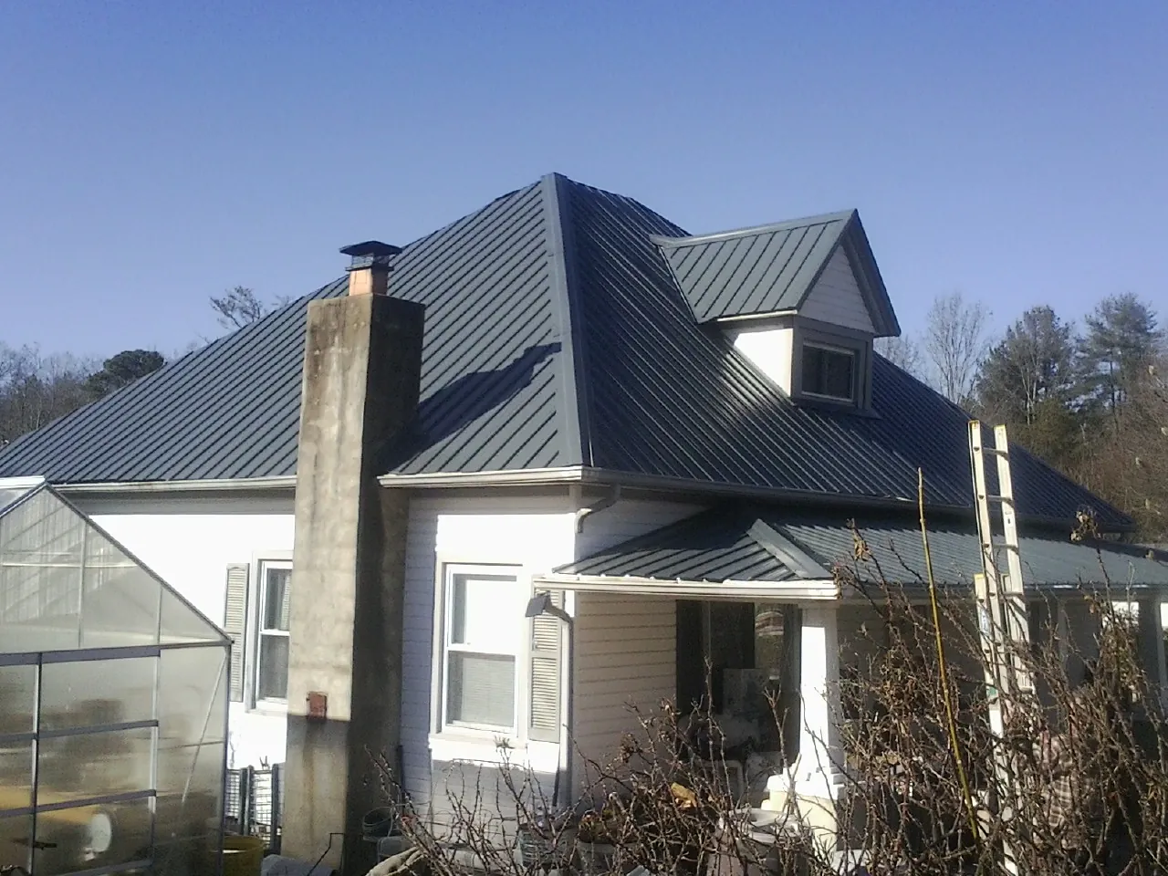Dark blue standing seam metal roof on a white farmhouse with dormer — Slate & Tile Roof Repair by Roofing Brothers in Dodge City