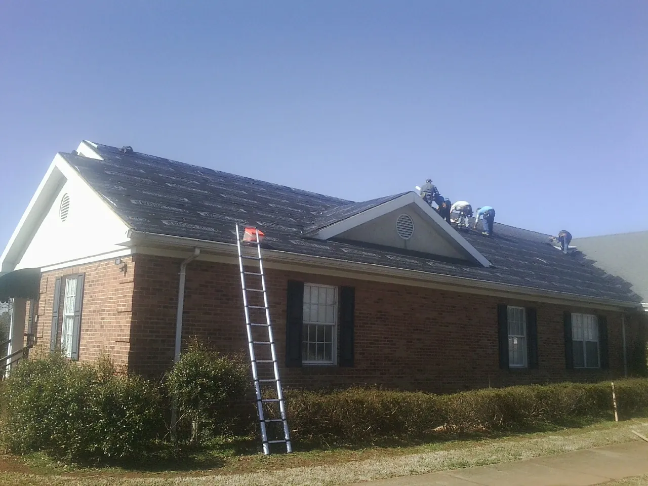Crew tearing shingles off a brick ranch roof with a ladder set — Emergency Roof Repair work by our crew in Dodge City