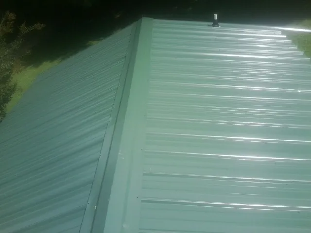 New green metal panels meeting at the ridge of a roof — Flat Roof Repair work by our crew in Dodge City
