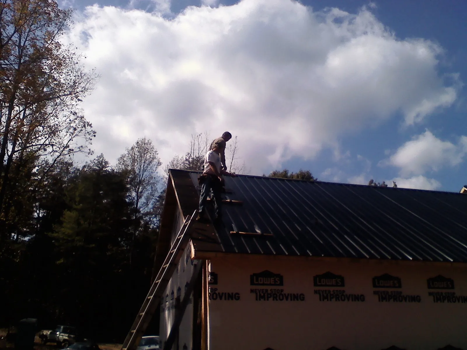Roofer fastening dark metal panels high against a cloudy sky, from a Roof Inspection job in Dodge City