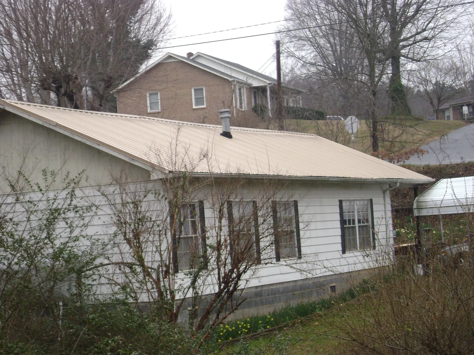 Tan metal roof on a white sided house set into a hillside — Commercial Roofing by Roofing Brothers in Dodge City