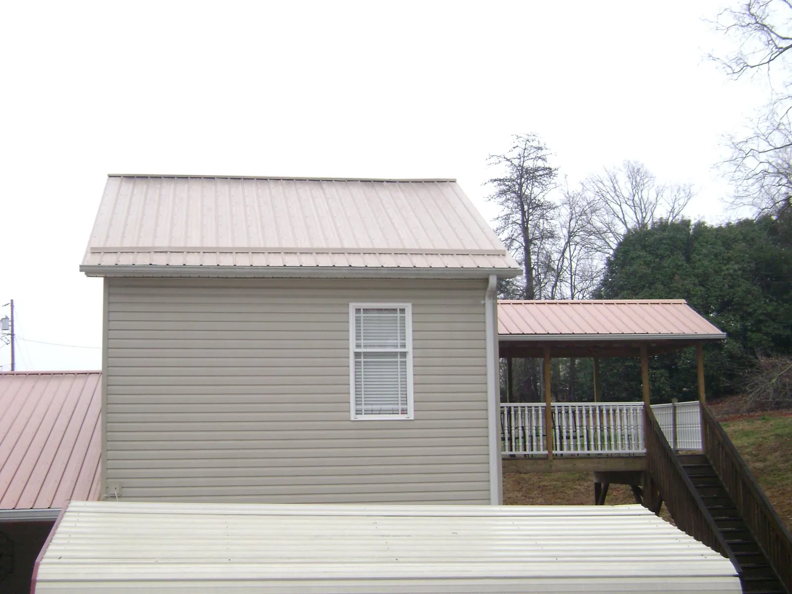 Tan metal roofs on a two story addition and attached porch, from a Roof Replacement job in Dodge City